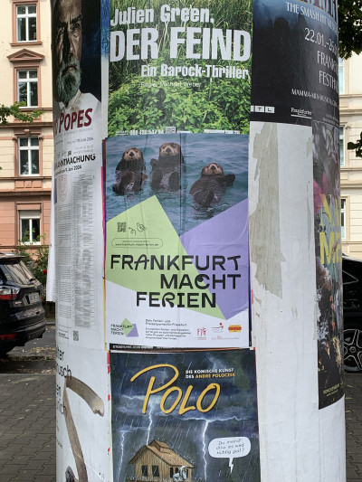 Plakatdesign an einer Litfaßsäule, auf dem Poster treiben drei winkende Otter auf dem Wasser, darunter steht Frankfurt macht Ferien